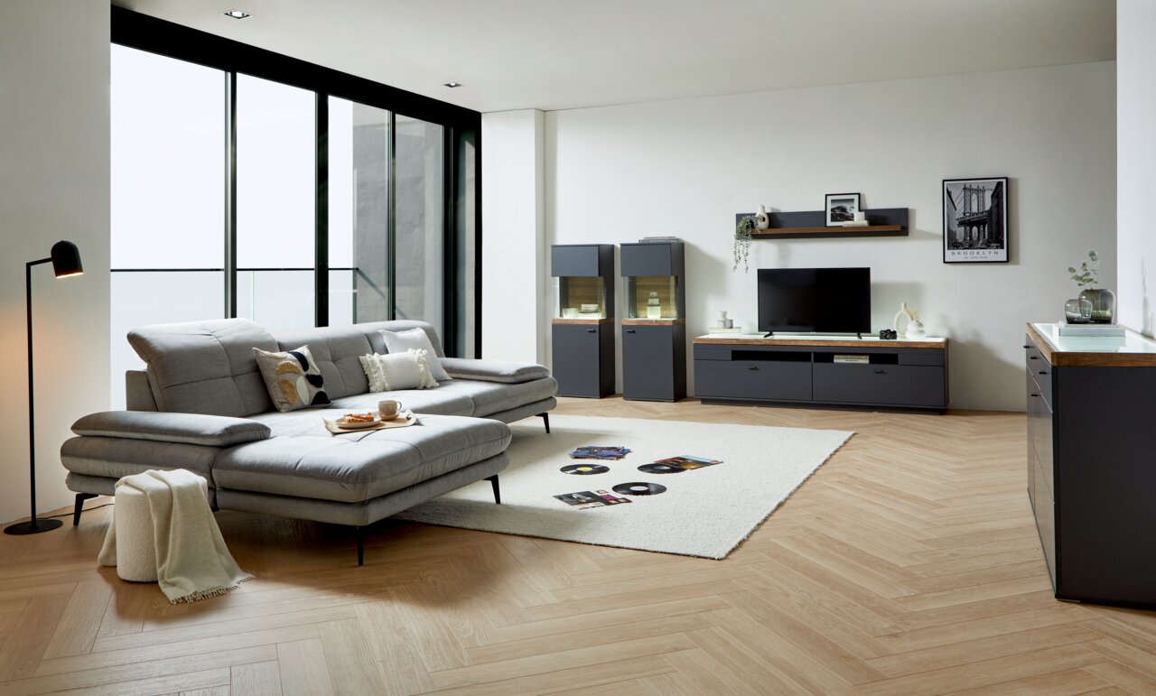 Modernes Wohnzimmer mit grauem Sofa, Couchtisch und TV-Lowboard in einer hellen, stilvollen Umgebung. Perspektive von der Seite.