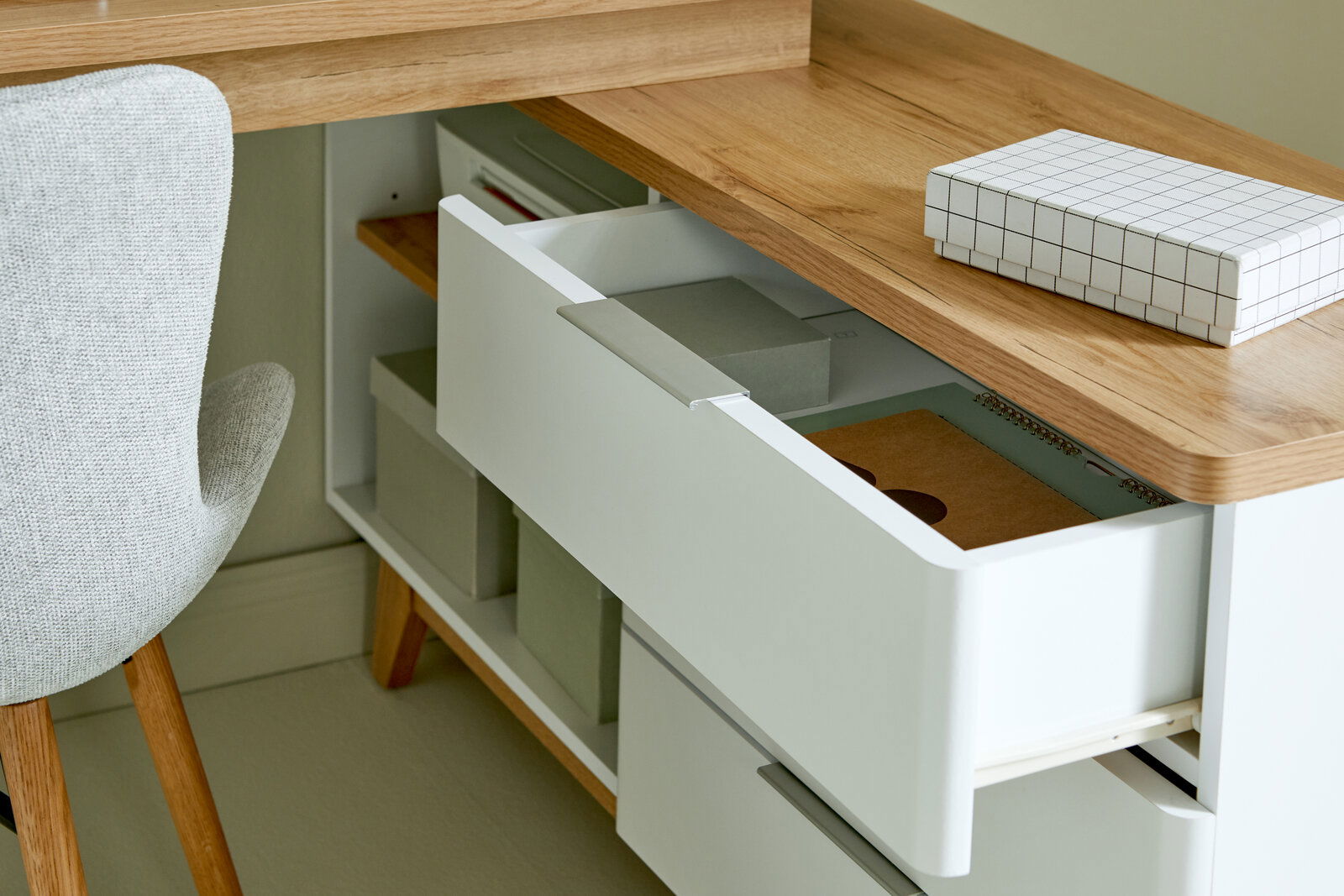 Nahaufnahme eines Eck-Schreibtisches mit Holzoberfläche, geöffneten Schubladen und einem grauen Stuhl von der Seite betrachtet.