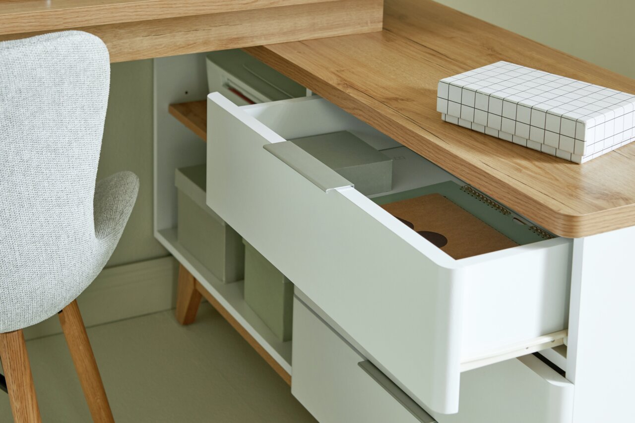 Nahaufnahme eines Eck-Schreibtisches mit Holzoberfläche, geöffneten Schubladen und einem grauen Stuhl von der Seite betrachtet.