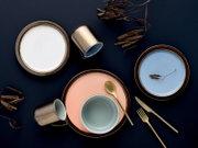 Keramikgeschirr-Set in Pastellfarben mit Tellern, Schale, zwei Tassen und goldenem Besteck auf dunkelblauem Hintergrund, Draufsicht (Flatlay)