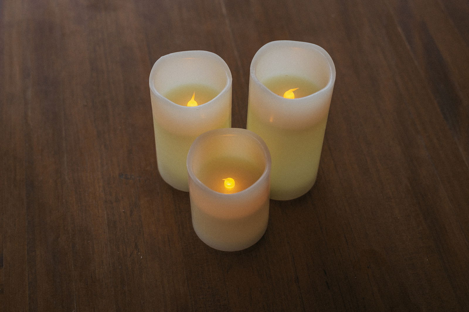 Drei Outdoor-Kerzen in verschiedenen Größen auf einem Holztisch, von oben betrachtet, mit warmem LED-Licht.