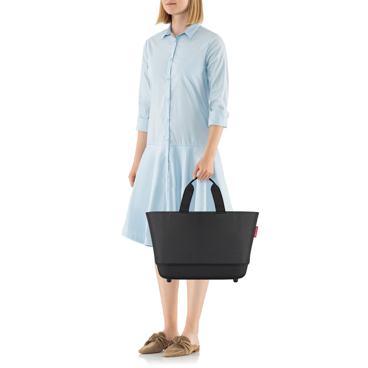 Reisenthel Shoppingbasket Black Frau in hellblauem Kleid hält einen schwarzen Einkaufskorb mit zwei Griffen, seitliche Perspektive