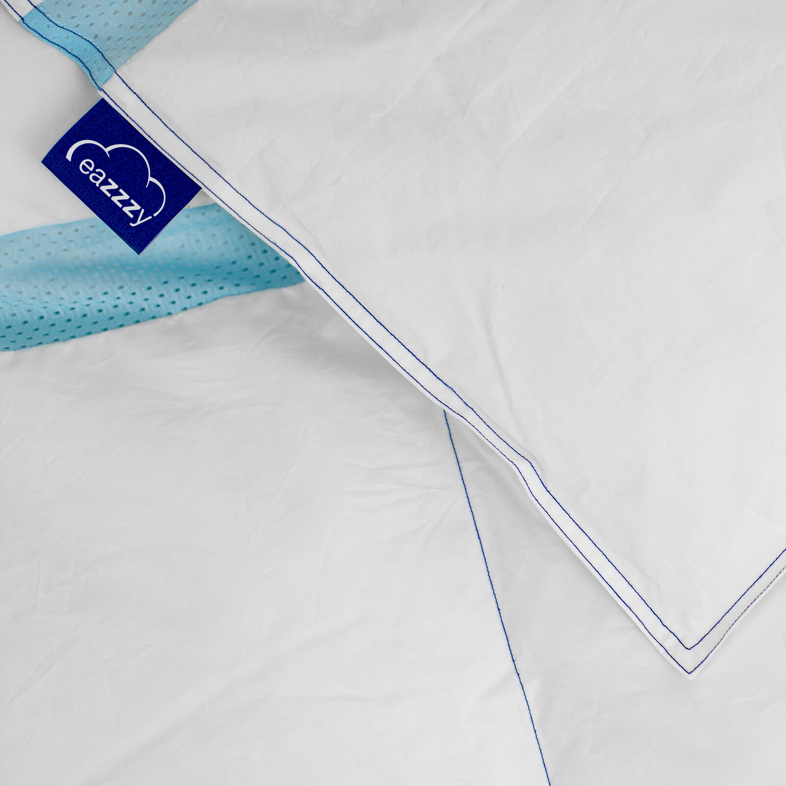 Nahaufnahme einer weißen Bettdecke mit blauer Paspelierung und türkisfarbenem, perforiertem Einsatz; eazzzy-Label sichtbar, Ansicht von oben (Top-Down).