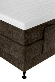Close-up in schuin bovenaanzicht van een bruin gestoffeerd boxspringbed met een wit, golvend doorgestikt matras en zwarte poot
