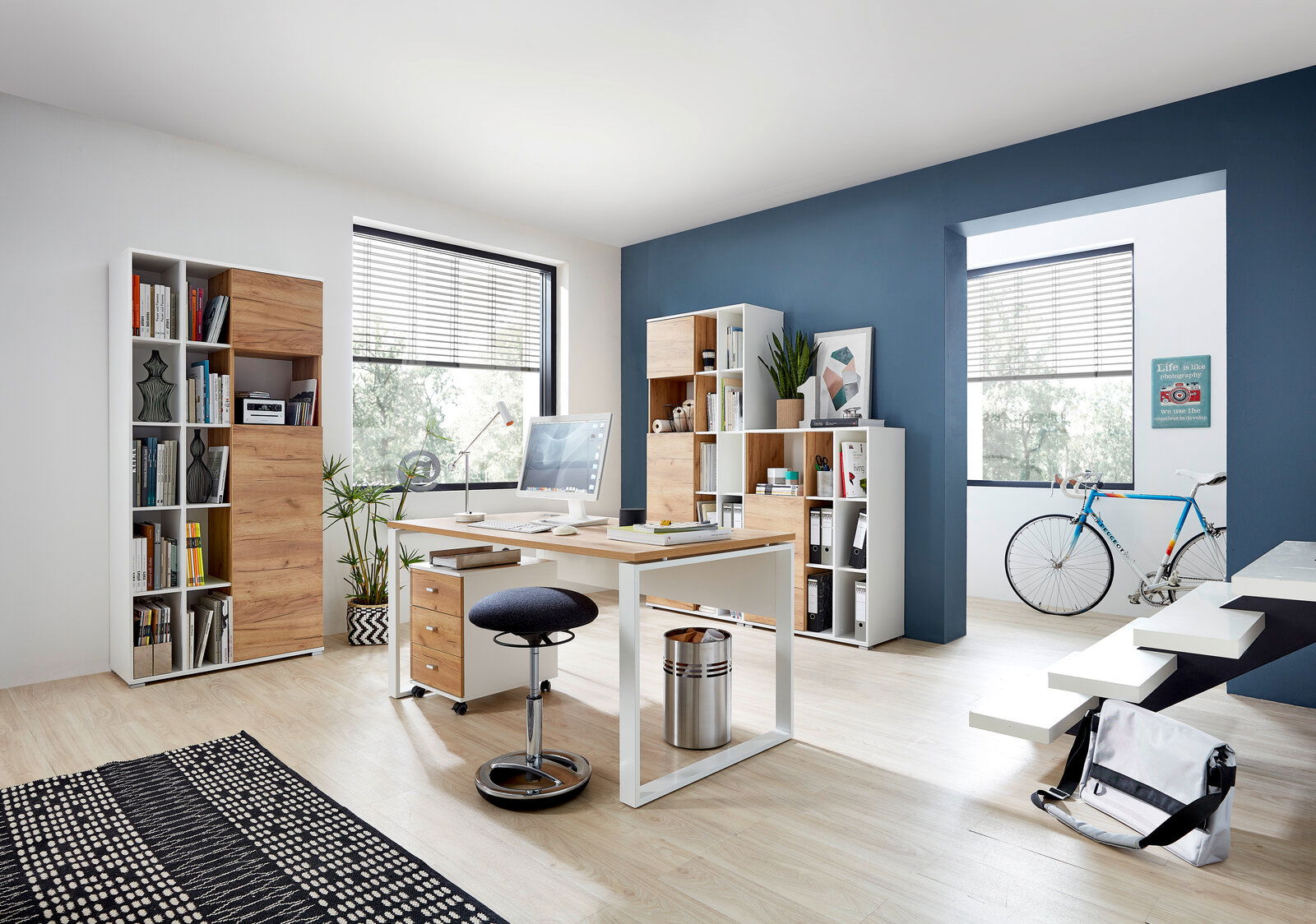 Moderner Büroraum mit Schreibtisch, Rollcontainer und Aktenschränken in Holz- und Weißtönen, seitliche Perspektive.