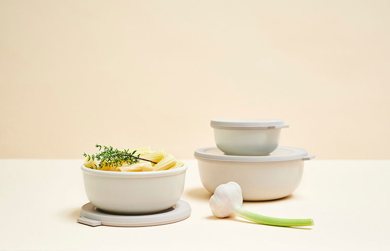 Multischüssel-Set 3-tlg. flach, bestehend aus drei unterschiedlich großen Schüsseln mit Deckeln, gefüllt mit geschnittenem Gemüse und Kräutern, aus seitlicher Perspektive fotografiert.