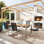 Moderner Gartentisch mit Holzplatte und Metallgestell, umgeben von sechs stilvollen Stühlen auf einer Terrasse mit Blick auf einen Pool und eine Außenküche.