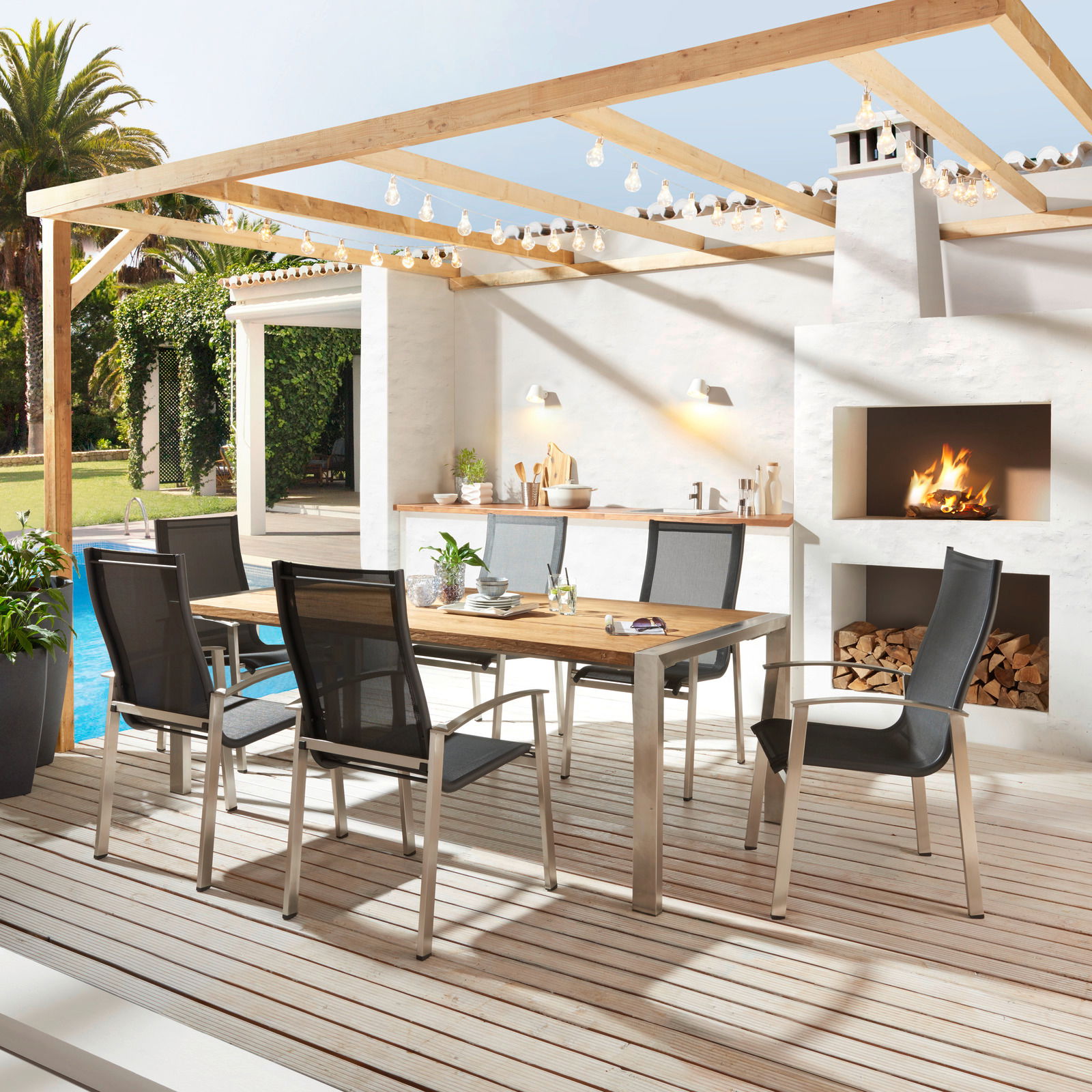 Moderner Gartentisch mit Holzplatte und Metallgestell, umgeben von sechs stilvollen Stühlen auf einer Terrasse mit Blick auf einen Pool und eine Außenküche.