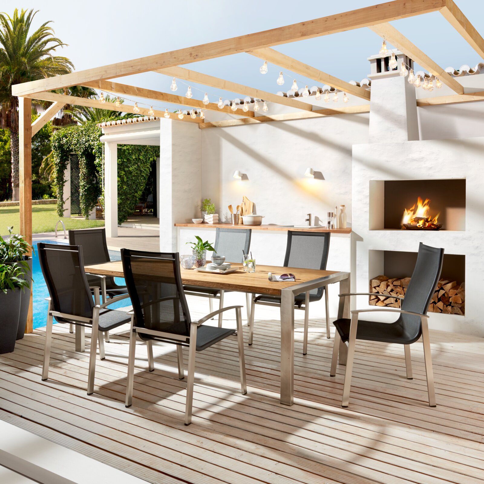 Moderner Gartentisch mit Holzplatte und Metallgestell, umgeben von sechs stilvollen Stühlen auf einer Terrasse mit Blick auf einen Pool und eine Außenküche.