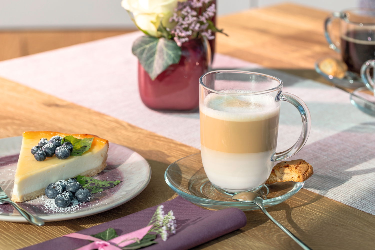 Leonardo Untertasse NAPOLI Untertasse Napoli 14,3cm mit Glas, gefüllt mit Latte Macchiato, von oben fotografiert, neben einem Stück Käsekuchen mit Blaubeeren und einem Keks.