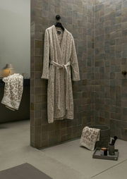 Beiger Bademantel mit Leopardenmuster, aufgehängt an einer Wand in einem stilvollen Badezimmer, seitliche Perspektive.