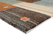 Nahaufnahme eines Frisé-Teppichs mit geometrischem Muster in Braun-, Beige- und Blautönen, perspektivisch von der Seite aufgenommen.