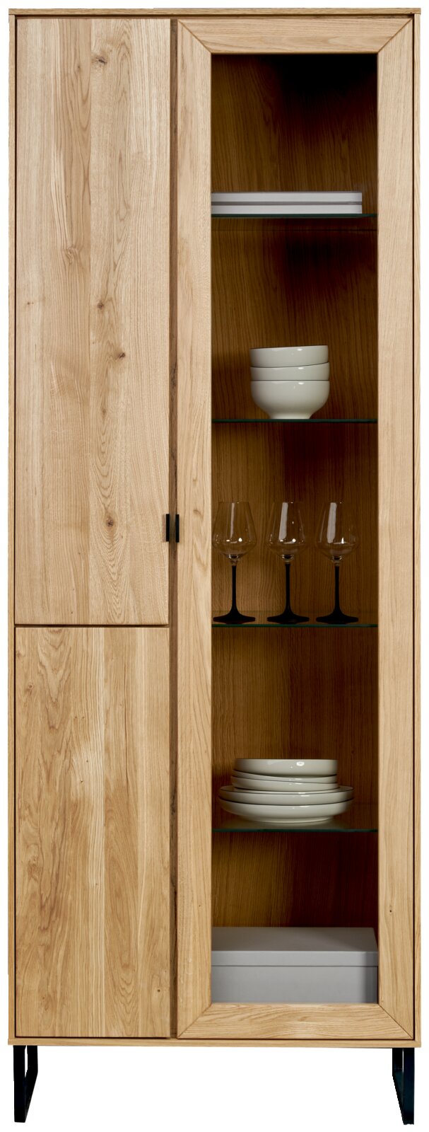 Hoge houten vitrinekast met deels gesloten deur links en glazen deur rechts met glazen legplanken en servies, frontaal aanzicht