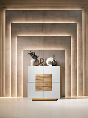 Moderne weiße Kommode/Sideboard mit Holz-Akzentfront und Holzsockel, dekoriert mit Vasen, vor beleuchteter Wandnische – Frontalansicht.