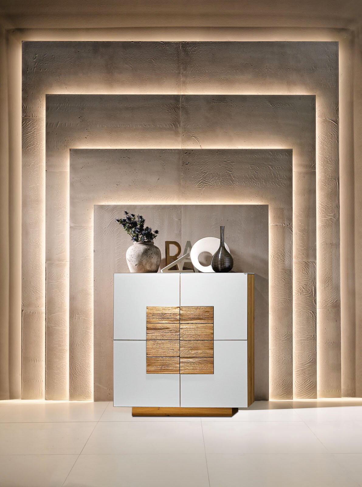 Moderne weiße Kommode/Sideboard mit Holz-Akzentfront und Holzsockel, dekoriert mit Vasen, vor beleuchteter Wandnische – Frontalansicht.