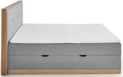 Zijaanzicht van een grijs boxbed met houten frame en wit matras.