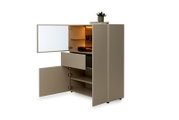 Moderner taupefarbener Hochschrank mit geöffneten Türen, ausgezogener Schublade, Glasboden und warm beleuchtetem Innenfach, aus schräger Vorderansicht