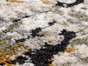 Nahaufnahme eines Designer Teppichs mit flauschiger Textur und einem Muster in Weiß, Grau, Schwarz, Grün und Orange, aus seitlicher Perspektive.