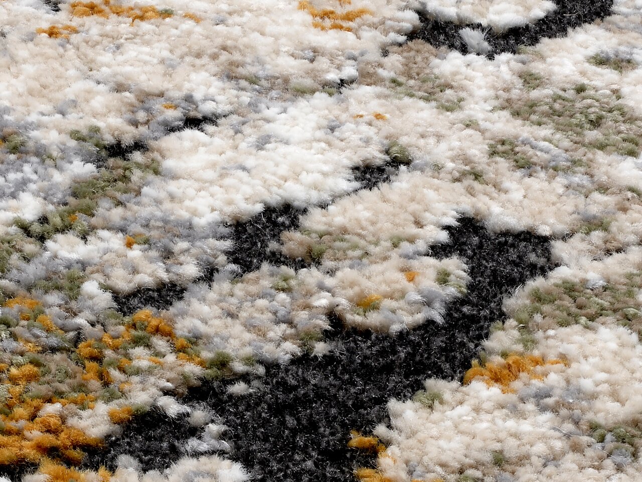 Nahaufnahme eines Designer Teppichs mit flauschiger Textur und einem Muster in Weiß, Grau, Schwarz, Grün und Orange, aus seitlicher Perspektive.