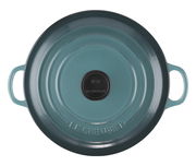 Vogelperspektive auf einen runden, blauen Bräter mit zwei Griffen und einem schwarzen Knauf, Marke Le Creuset.