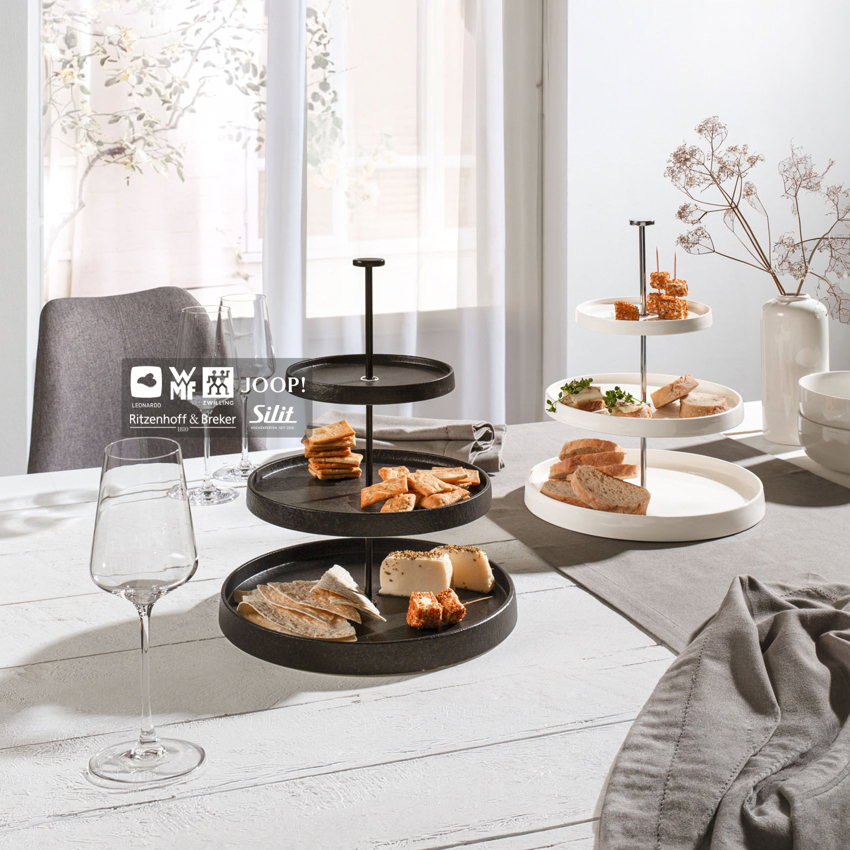 Moderne schwarze und weiße Etagèren mit stilvoll arrangierten Snacks und Gläsern auf hellem Esstisch.