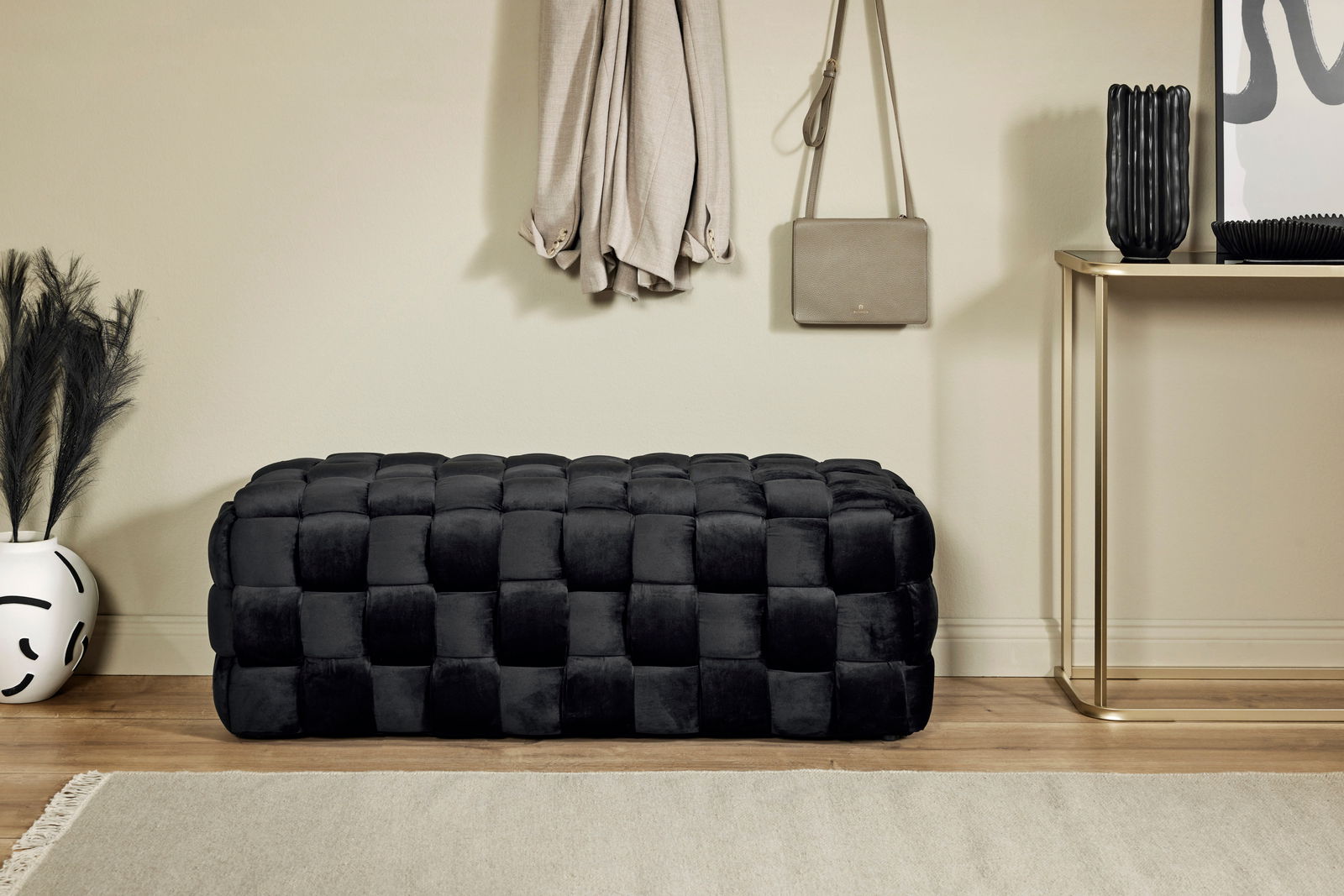 Schwarzer, gepolsterter Hocker in rechteckiger Form, aus seitlicher Perspektive fotografiert, in einem stilvoll eingerichteten Raum.