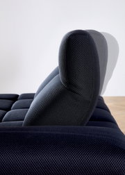 Zijaanzicht van een verstelbare hoofdsteun van een donkerblauwe hoekbank met gestructureerde stoffen bekleding.