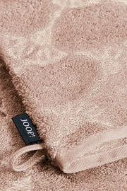 Nahaufnahme eines beigen Waschhandschuhs mit weicher Textur und einem schwarzen Etikett mit der Aufschrift 'JOOP!'