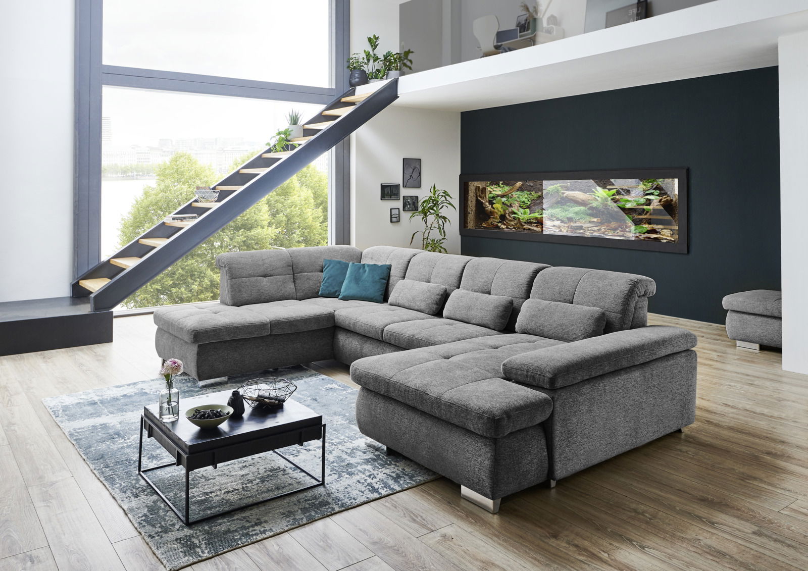 Graue Polsterrundecke Beldomo Style BOCHUM in einem modernen Wohnzimmer mit großen Fenstern und Treppe, seitliche Perspektive.