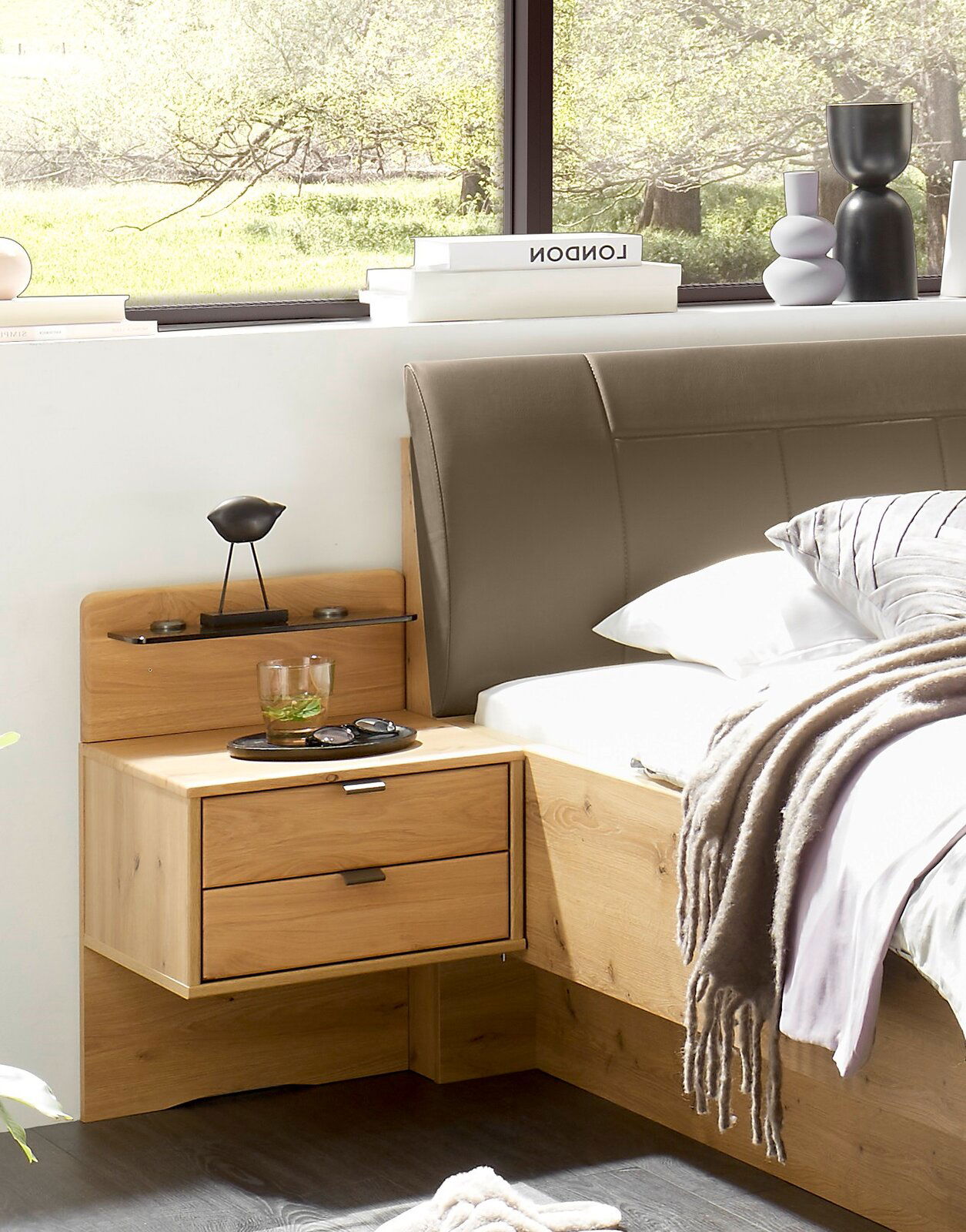 Linea Natura Nachtkonsolen-Paneele (Paar) CARDIFF Modernes Holzbett mit gepolstertem grauem Kopfteil und integriertem Nachttisch mit zwei Schubladen, dekoriert mit Glas und Dekoobjekten; Perspektive: seitliche Nahaufnahme von schräg vorn rechts.