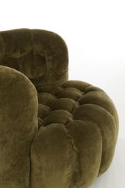 Nahaufnahme eines grünen Sessels mit weicher, gepolsterter Oberfläche und runder Form, seitliche Perspektive.