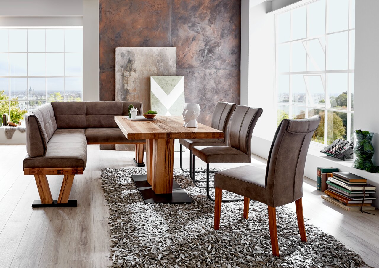 Moderner Esstisch aus Holz mit passender Eckbank und Stühlen in einem hellen Raum, seitliche Perspektive.