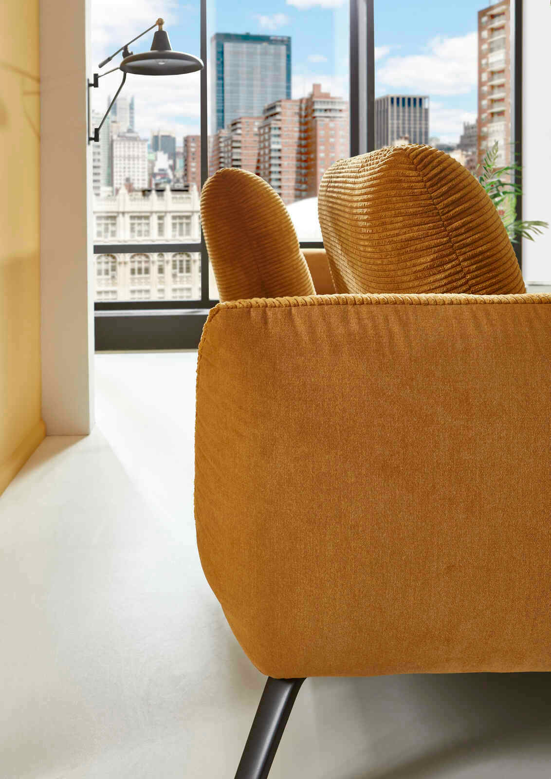 Nahaufnahme einer senfgelben Rundecke mit modernen schwarzen Beinen, im Hintergrund eine städtische Skyline durch ein großes Fenster sichtbar.