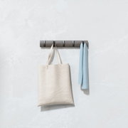Moderne Wandgarderobe mit mehreren Haken, an der eine beige Tasche und ein hellblaues Tuch hängen, frontal betrachtet.