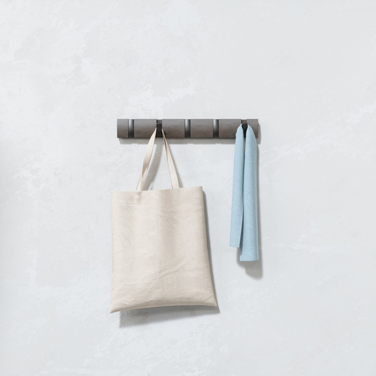 Moderne Wandgarderobe mit mehreren Haken, an der eine beige Tasche und ein hellblaues Tuch hängen, frontal betrachtet.