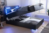 Boxspringbett mit hochgeklappter Matratze, darunter Stauraum mit Kissen und Decken, LED-Beleuchtung am Kopfteil, seitliche Perspektive.