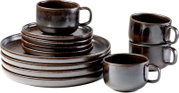 Rustikales Keramik-Geschirrset in dunkler braun-grauer Glasur mit Tellern, Untertassen und Kaffeetassen, schräg von vorn in Studioansicht fotografiert