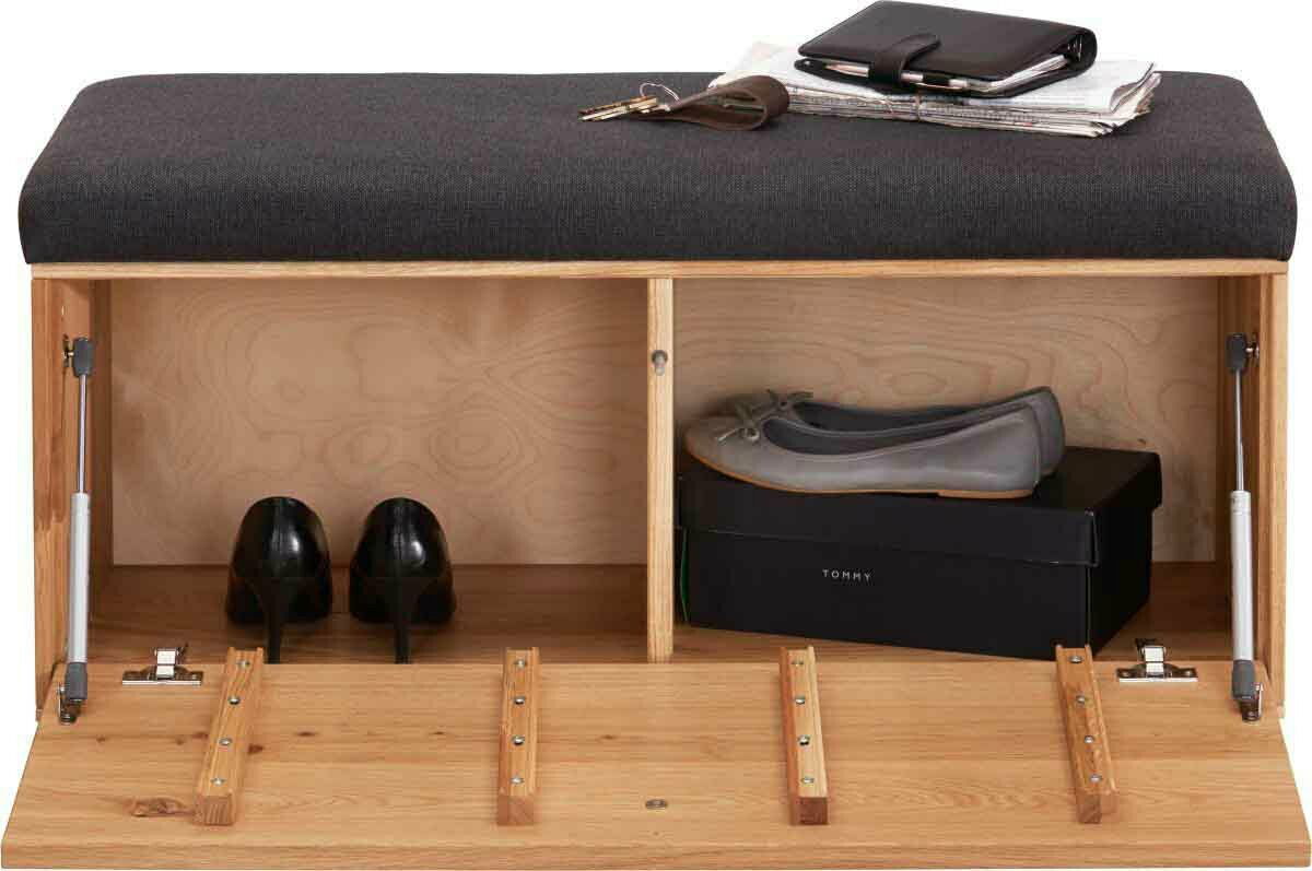 Garderobenbank mit gepolsterter Sitzfläche in dunklem Stoff, darunter Stauraum mit Schuhen und einer Schuhschachtel, aus hellem Holz, Perspektive von vorne.