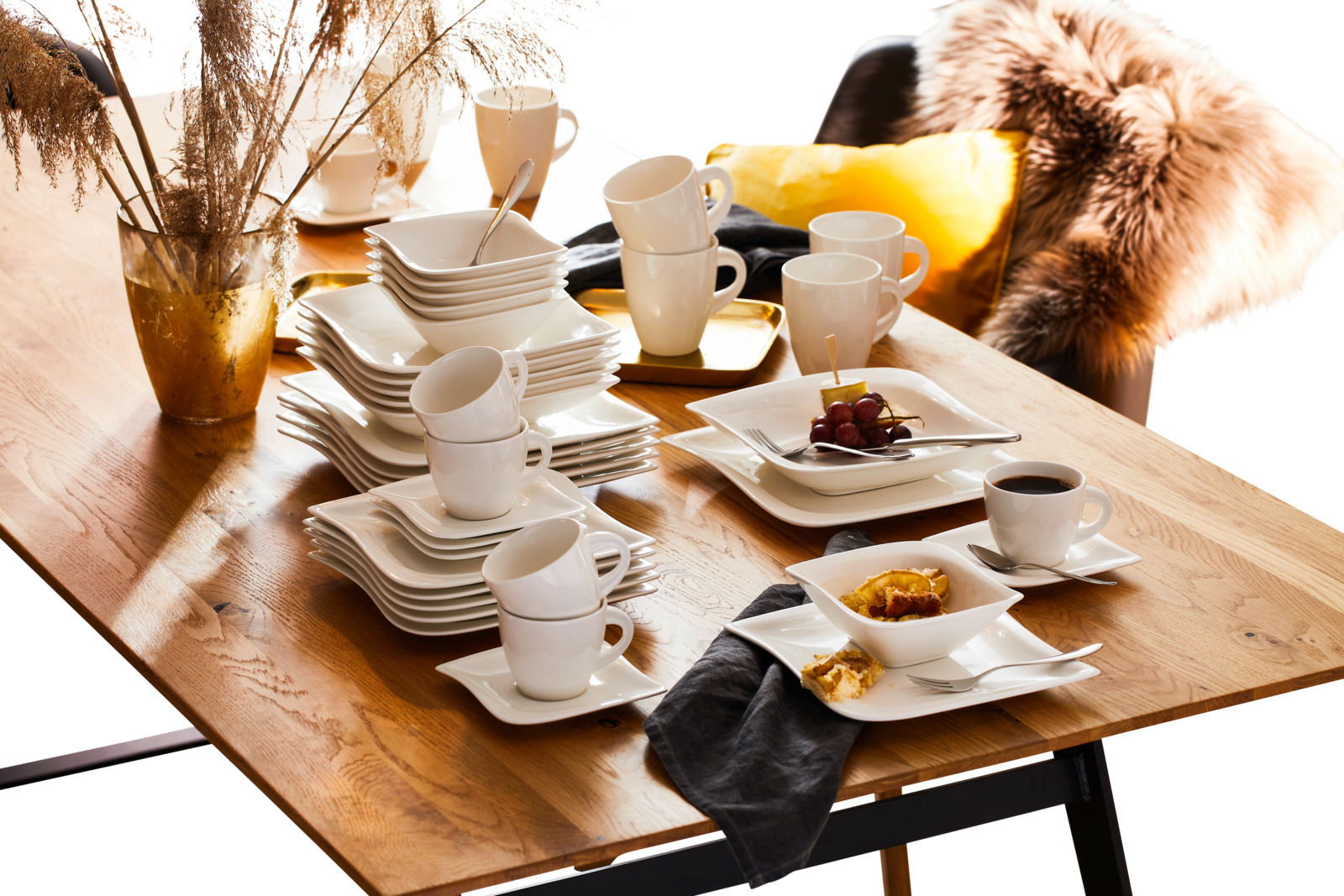 Elegantes Kombiservice La Musica 42-tlg. auf einem Holztisch, mit gestapelten Tellern, Tassen und Schalen, aus seitlicher Perspektive fotografiert.