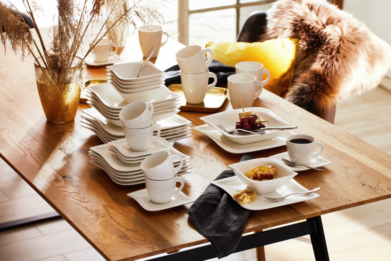 Elegantes Kombiservice La Musica 42-tlg. auf einem Holztisch, mit gestapelten Tellern, Tassen und Schalen, aus seitlicher Perspektive fotografiert.