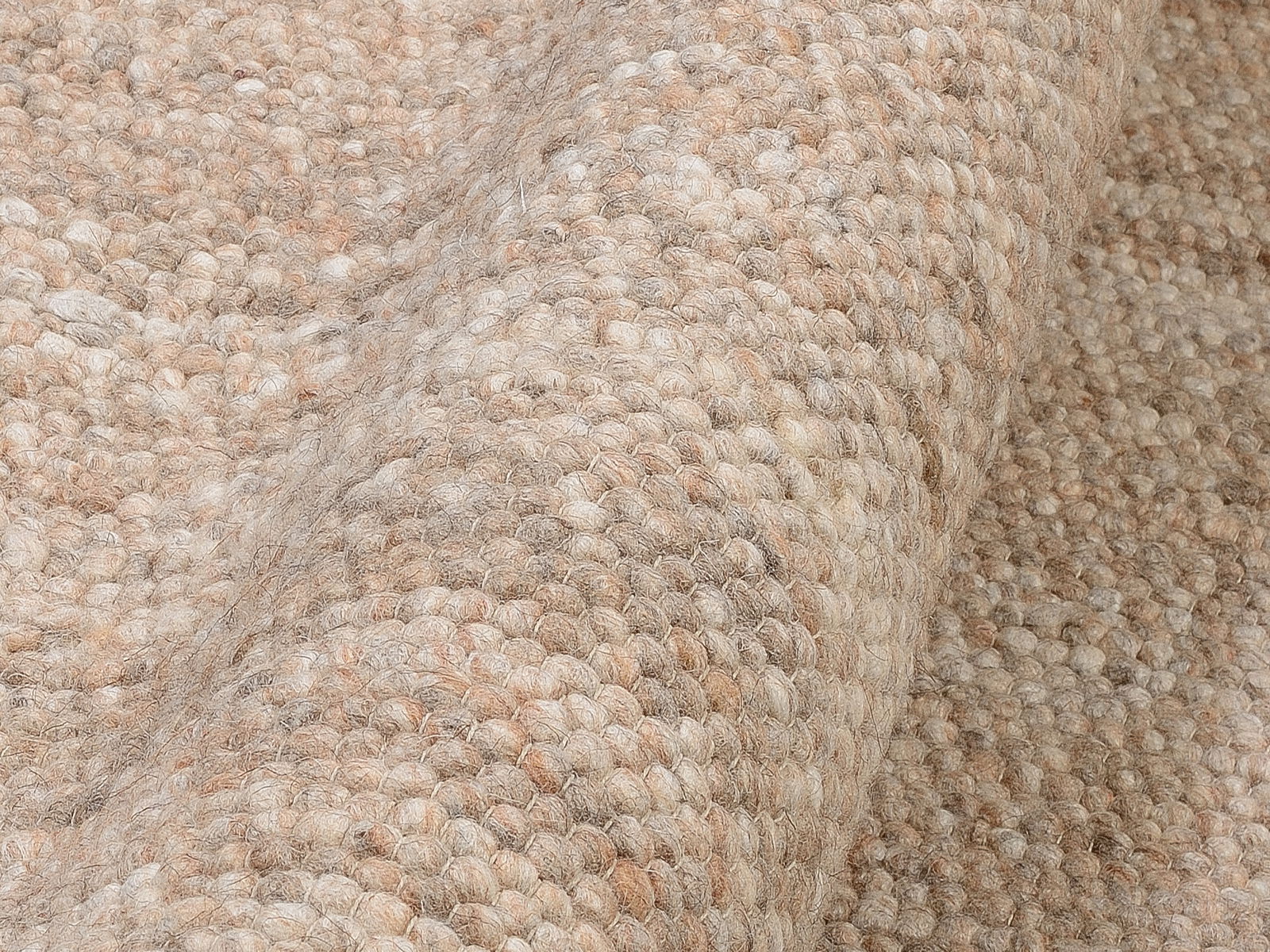 Nahaufnahme eines handgewebten Teppichs in natürlichen Beige- und Brauntönen, mit einer strukturierten, gewellten Oberfläche.