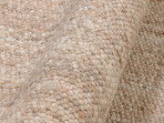 Nahaufnahme eines handgewebten Teppichs in natürlichen Beige- und Brauntönen, mit einer strukturierten, gewellten Oberfläche.