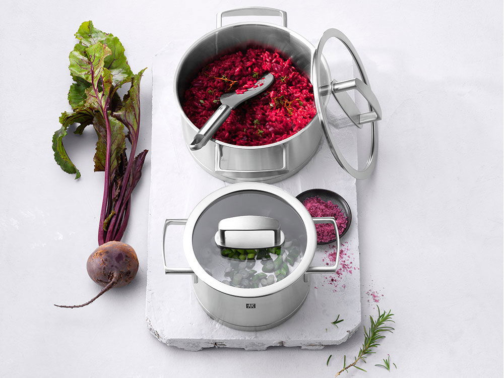 Zwei Edelstahltöpfe mit rotem Rote-Bete-Risotto und Kräutern, daneben eine frische Rote Bete.