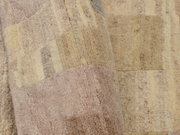 Nahaufnahme eines Wollteppichs mit geometrischem Muster in sanften Beige- und Rosatönen, aus seitlicher Perspektive aufgenommen.