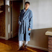 Mann in einem blauen Bademantel mit Schalkragen steht in einem Raum, frontal zur Kamera.