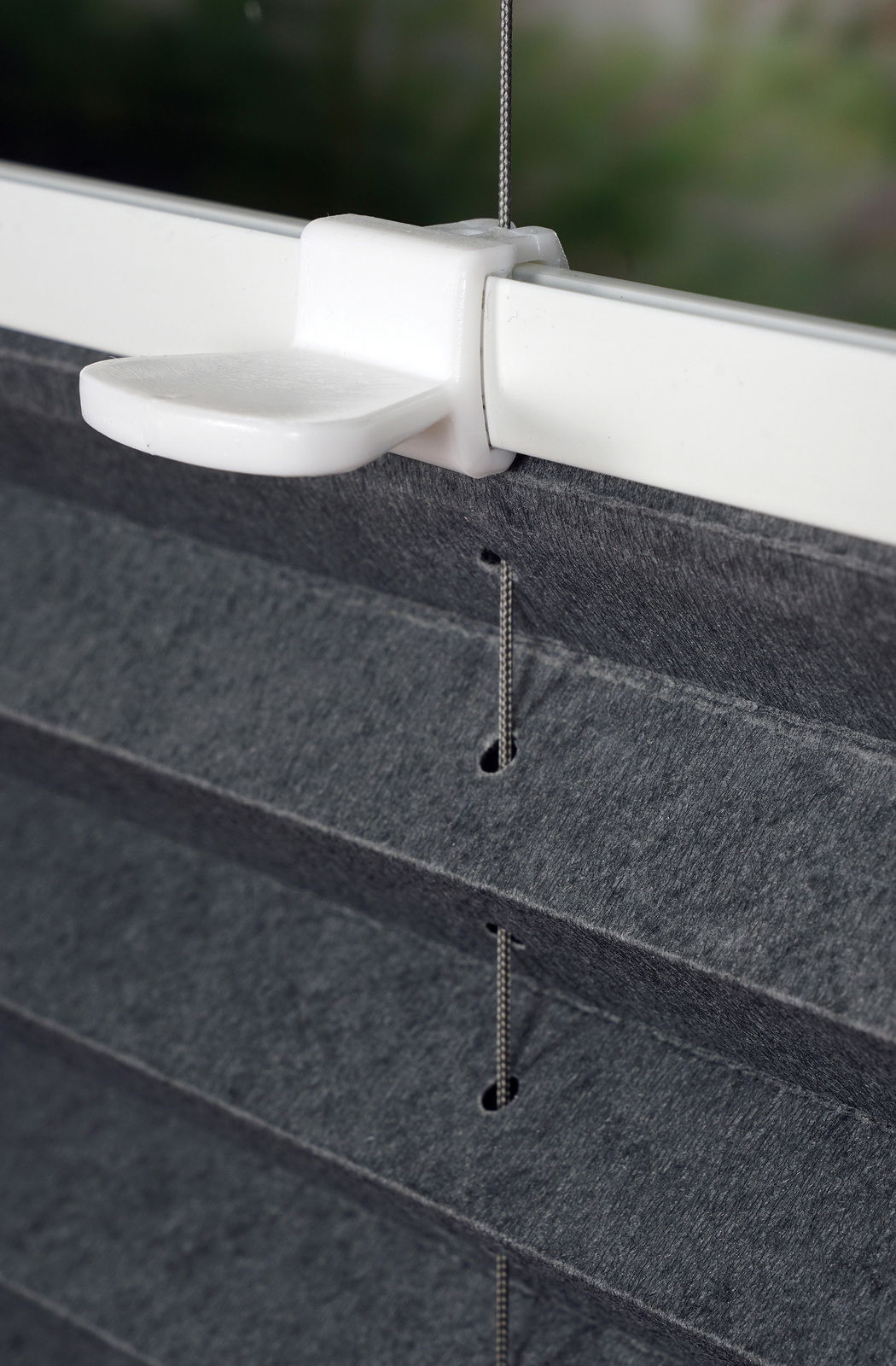 Nahaufnahme eines gefädelten Plissees in Anthrazit, montiert an einem Fensterrahmen. Die Perspektive zeigt die seitliche Ansicht der Fäden und der Halterung.