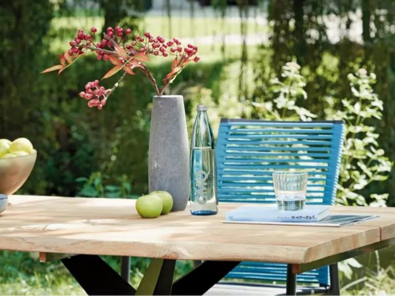 Eettafel voor buiten met houten blad, versierd met een vaas en rode bessen, een waterfles en een glas, zijaanzicht
