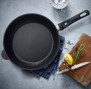 Schmorpfanne 28cm aus der Vogelperspektive auf einem Küchentisch mit Kräutern, Zitrone und Messer.