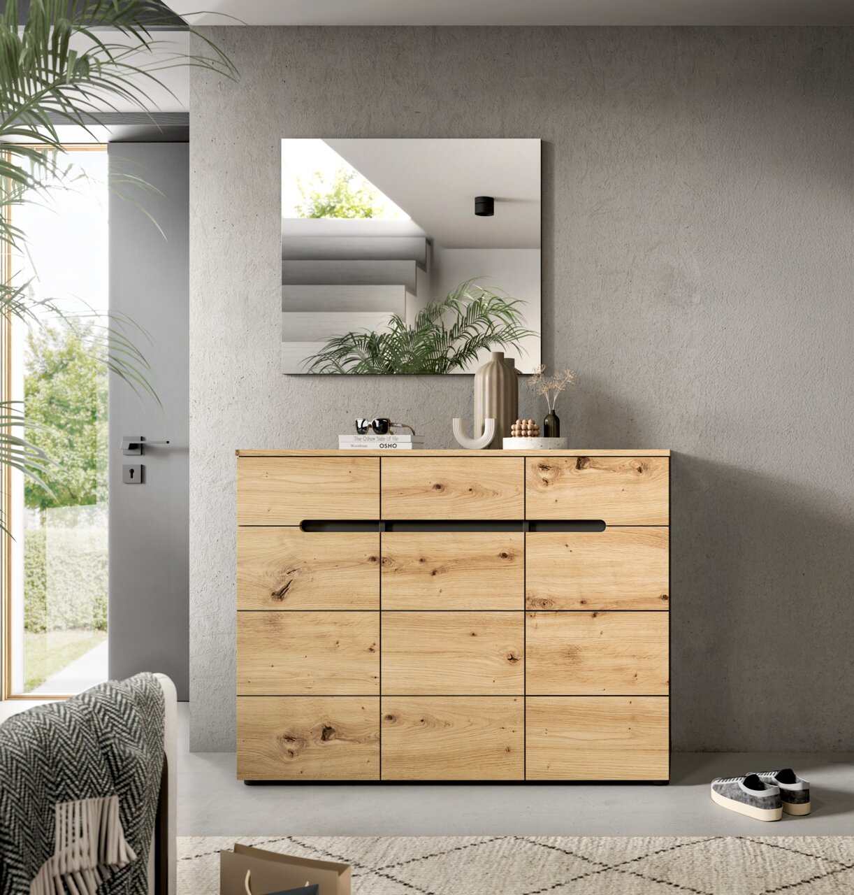 Moderne Holzkommode aus massiver Eiche mit markanter Maserung und schwarzen Griffleisten, frontal in einem hellen Wohnraum unter einem Wandspiegel inszeniert