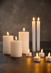 Verschiedene LED-Kerzen in unterschiedlichen Größen und Formen, die auf einem dunklen Untergrund leuchten. Die Perspektive zeigt die Kerzen von vorne.